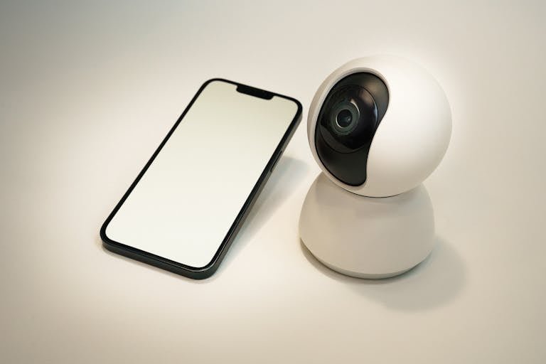 A modern smart home security camera next to a blank screen smartphone, showcasing home automation technology.